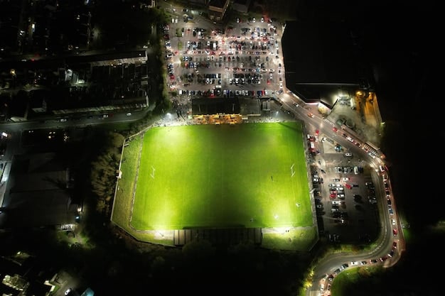 An overhead shot of a soccer stadium during a night game, with vibrant floodlights illuminating the pitch and blurred, energetic fans in the stands, showcasing the grand scale of the event.