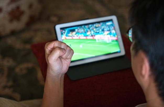 A person's hand holding a tablet displaying a live soccer match, with a blurred background of a living room, highlighting focused digital engagement.