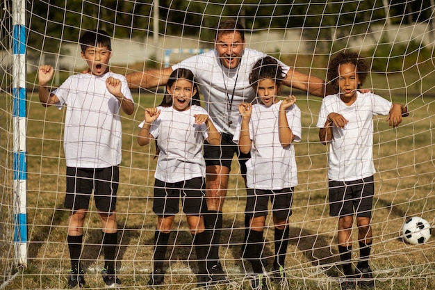 A diverse group of young soccer players, boys and girls, practicing soccer drills on a sunny day. They are wearing a mix of soccer jerseys from different clubs and national teams, representing the global nature of the sport. The focus is on teamwork and skill development.