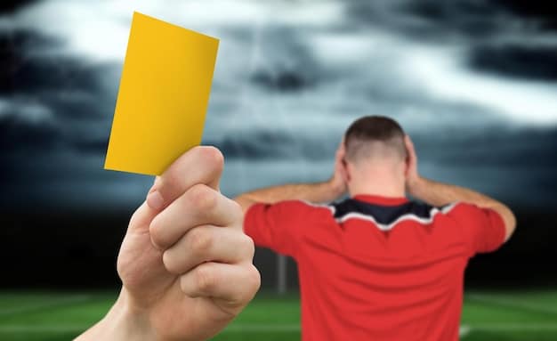 A close-up photograph of a referee holding a yellow card during a soccer match. The background is blurred, focusing attention on the referee's hand and the card. The overall tone is serious and conveys the importance of discipline in the sport. Visible sweat and determined eyes.